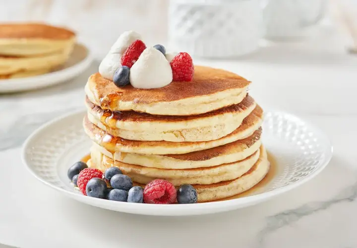 Pancakes dietetici con panna montata, mirtilli e lamponi, inzuppati nello sciroppo d'acero.