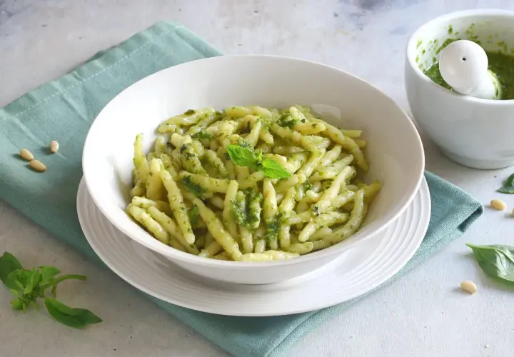 Un piatto di pasta al pesto fresco, con basilico e pinoli sparsi, pronto per essere gustato.