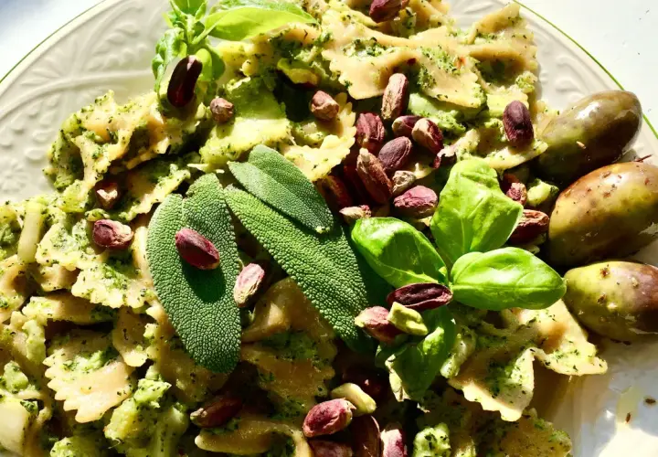 Farfalle condite con un saporito pesto di salvia, guarnite con pistacchi, basilico e olive verdi.