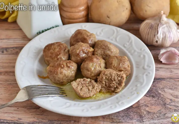 Polpette in umido succulente su un piatto bianco, con patate e aglio sullo sfondo. Una forchetta è pronta per gustarle.