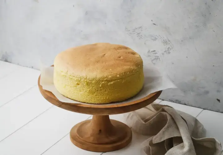 Una soffice torta con albumi, dorata e leggera, su un alzata di legno. Perfetta per una colazione o merenda.