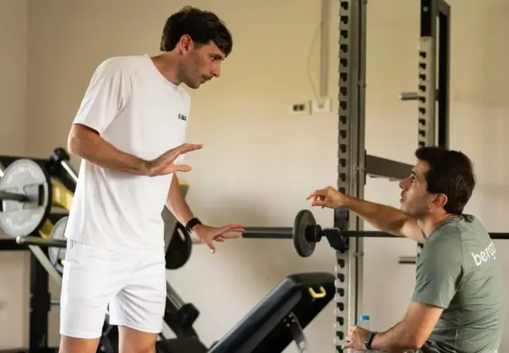 Due uomini discutono in palestra, uno in bianco, l'altro con maglia "bergamini padel".