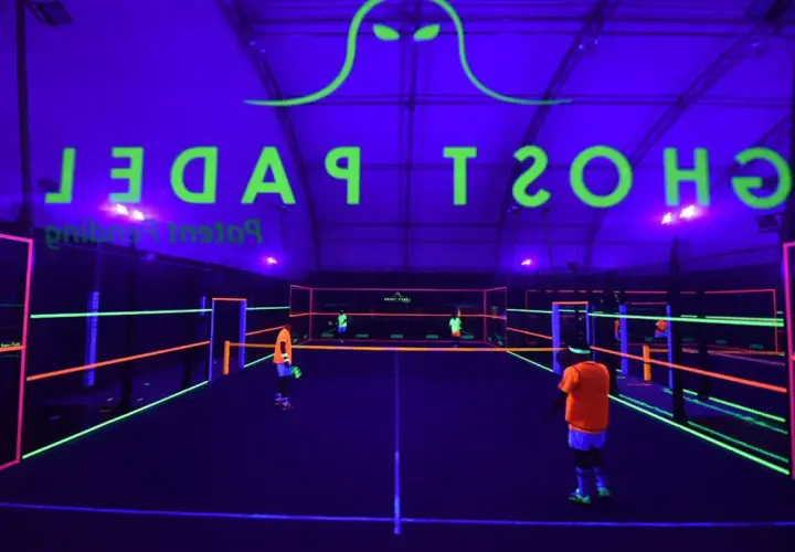 Campo da padel al neon con logo "Ghost Padel" e giocatori in azione.