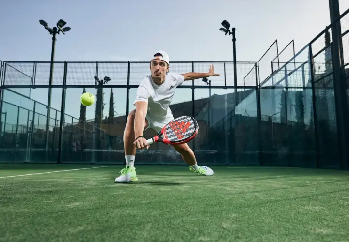 Ale Galán in azione, con le sue scarpe da padel che spiccano sul campo verde. Colpisce la palla con determinazione.