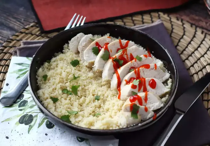 Delizioso pollo in padella a fette, servito su couscous e guarnito con salsa piccante e coriandolo fresco.