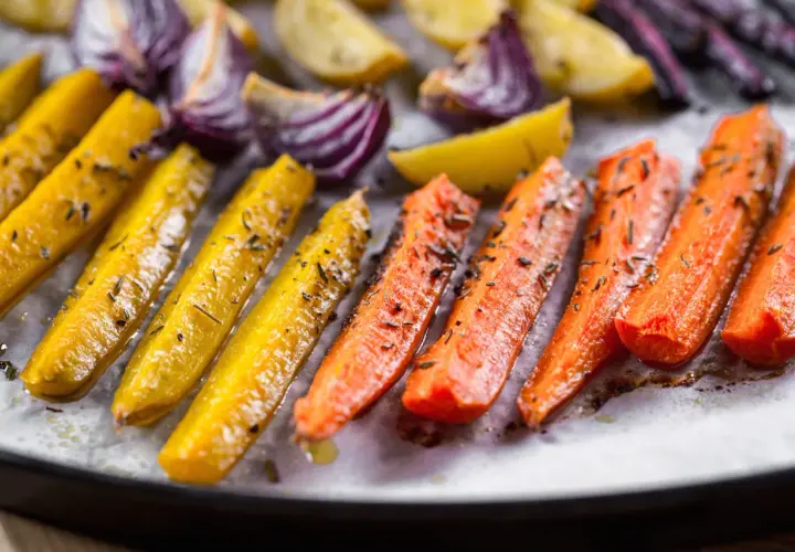Carote gialle e arancioni, cipolle rosse e patate dorate, condite con erbe aromatiche, pronte per essere gustate come deliziose verdure miste al forno.