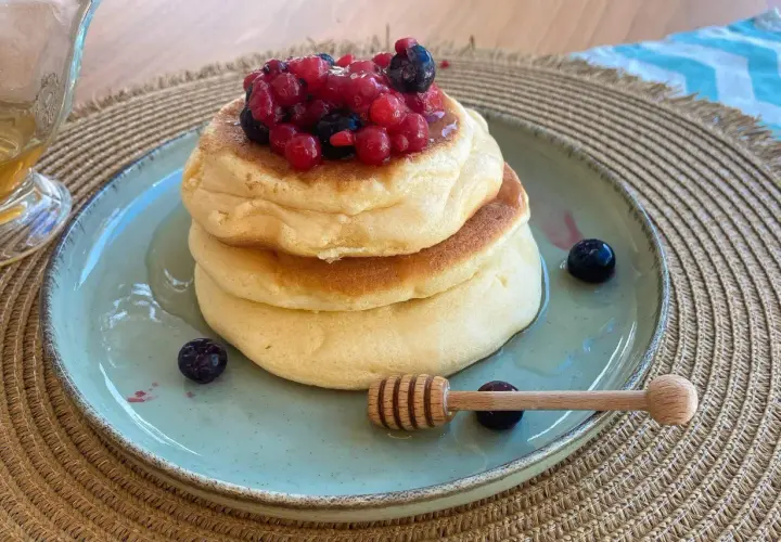 Pancake ricetta: soffici pancake impilati, guarniti con frutti di bosco e miele, pronti per essere gustati.