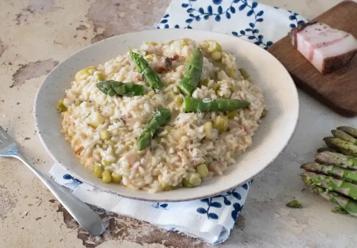 Un cremoso risotto con asparagi e pancetta, guarnito con punte di asparagi freschi e una spolverata di parmigiano.