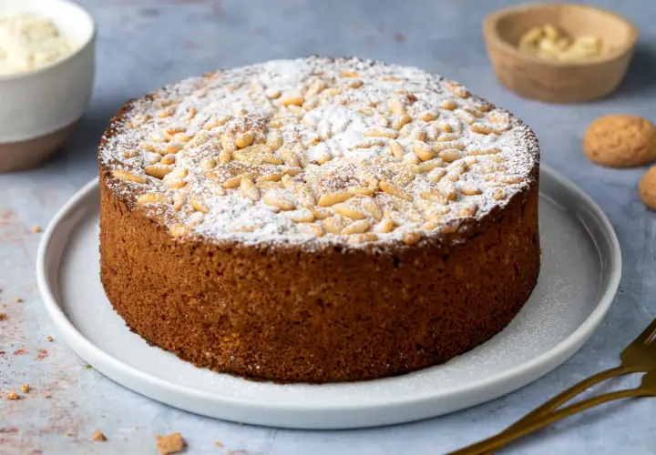 Torta soffice con farina di mandorle, cosparsa di pinoli e zucchero a velo.