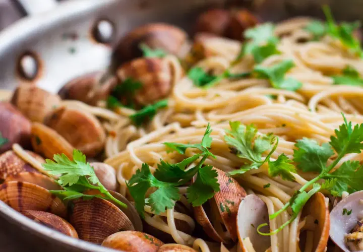 Spaghetti alle vongole surgelate, un piatto gustoso con pasta, cozze e prezzemolo fresco in una padella.