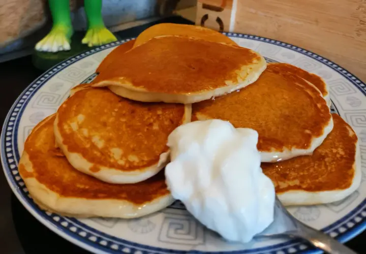 Pancake senza uova con yogurt, una pila dorata su un piatto decorato, pronta per essere gustata.