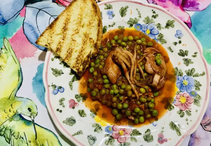 Piatto di totani con piselli in umido, accompagnato da una fetta di pane abbrustolito, su un piatto decorato con fiori e uccelli.