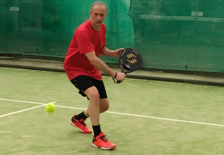 Uomo in campo da padel, pronto a colpire la palla. Un momento di gioco intenso nel padel Italia.