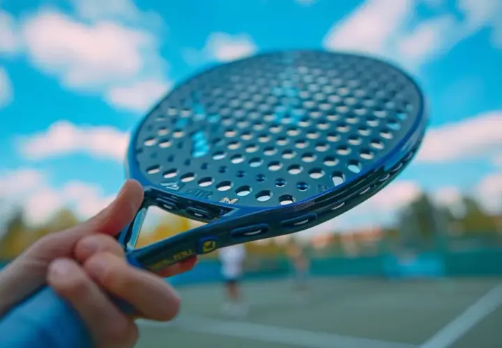 Racchette padel controllo: impugnatura blu di una racchetta da padel con campo e cielo sullo sfondo.