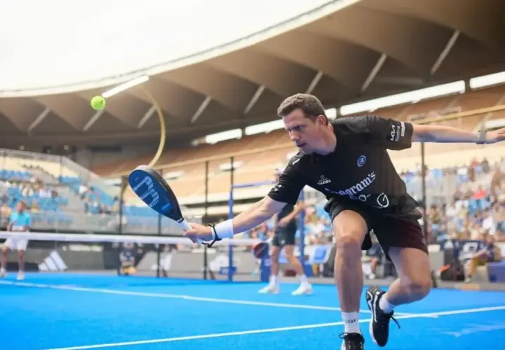 Paquito Navarro in azione, colpisce la palla con la racchetta da padel su un campo blu, con il pubblico sugli spalti.