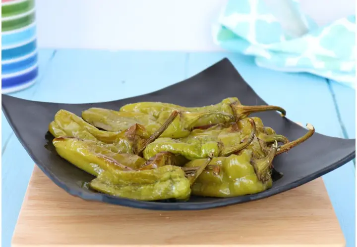 Friggitelli al forno, verdi e succosi, serviti su un piatto nero. Un contorno semplice e gustoso.