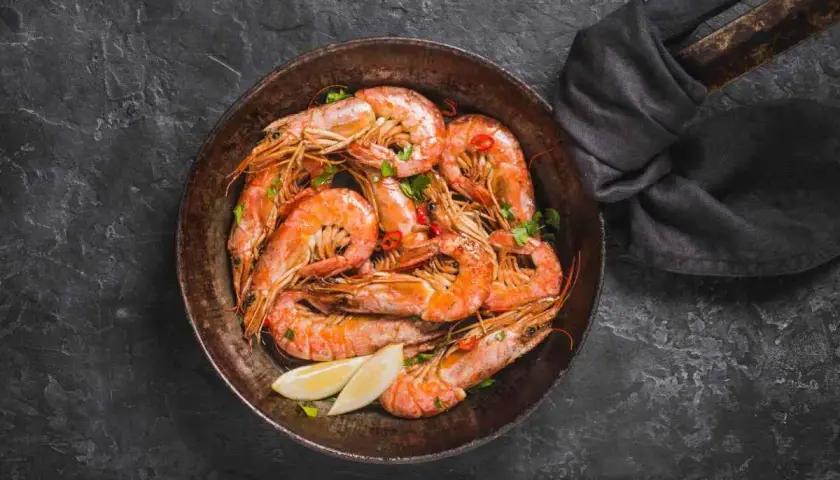 Gamberi in padella, succulenti e profumati, pronti per essere gustati con spicchi di limone fresco e un tocco di peperoncino.