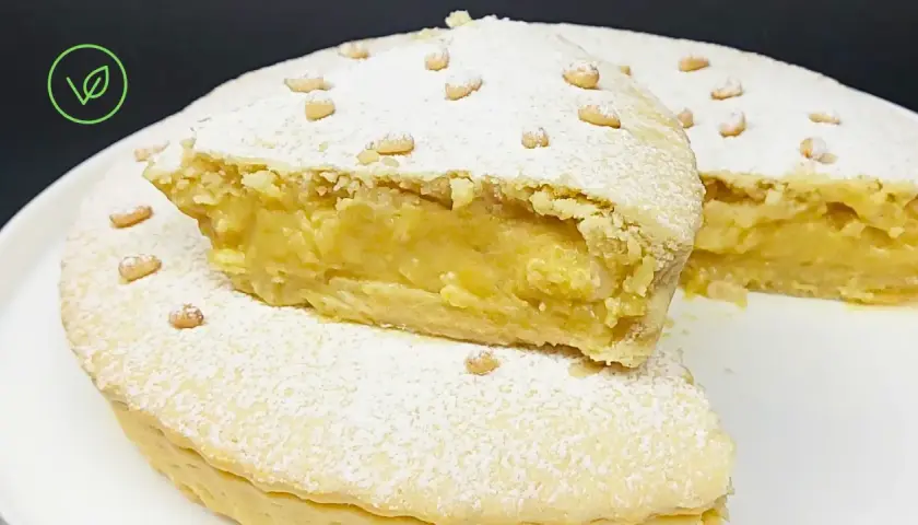 Torta vegana con crema gialla, ricoperta di zucchero a velo e pinoli. Un dolce delizioso e invitante.