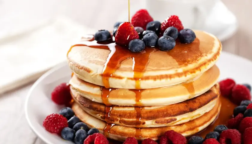 Pancakes con farina di avena, guarniti con frutti di bosco freschi e sciroppo d'acero che cola.