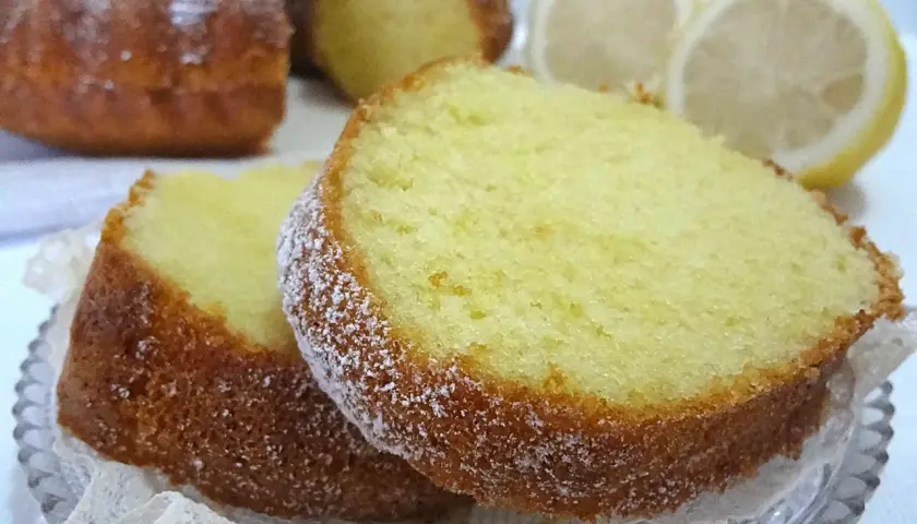 Fette di ciambellone al limone spolverate di zucchero a velo, con spicchi di limone sullo sfondo.