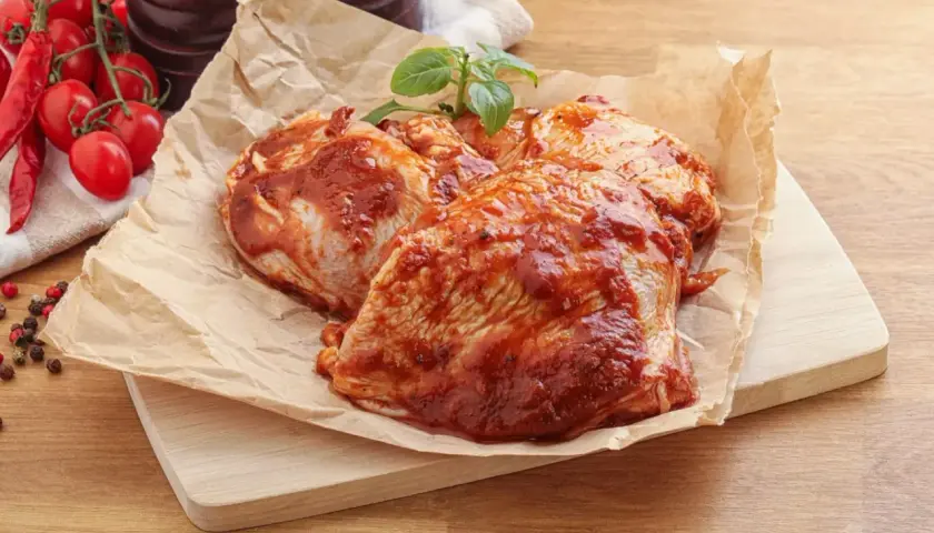 Cosce di pollo pronte per la marinatura, con pomodorini e peperoncino sullo sfondo.