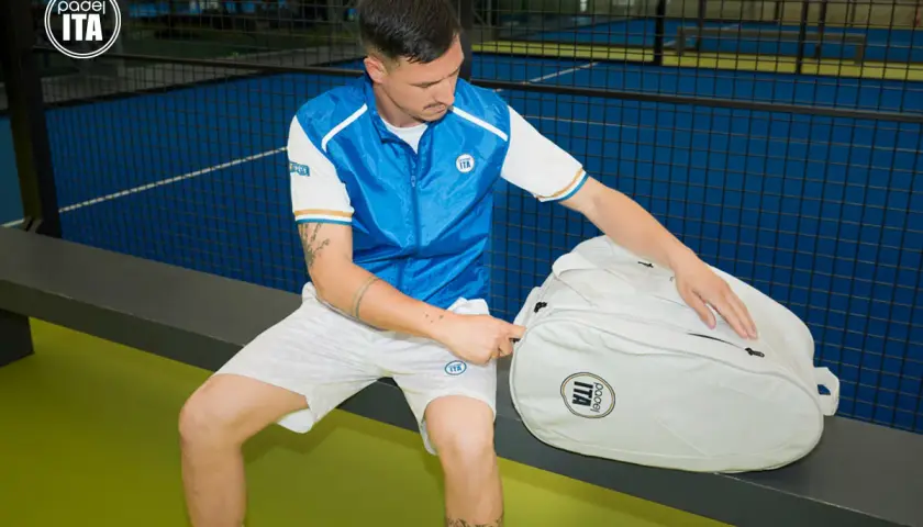 Un giocatore di padel con abbigliamento sportivo bianco e blu, pronto per giocare. Scopri come vestirsi per giocare a padel con stile e comfort.