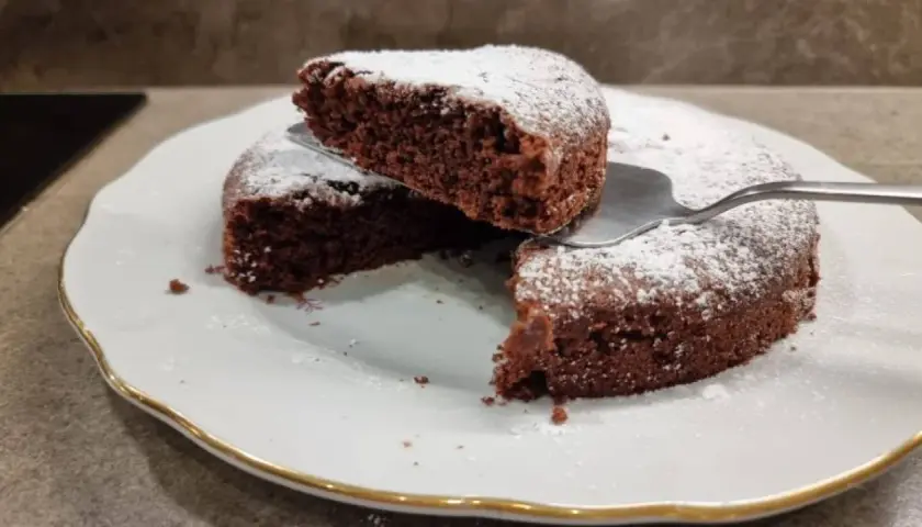 Una fetta di torta all'acqua al cacao, soffice e spolverata di zucchero a velo, viene sollevata da una paletta.