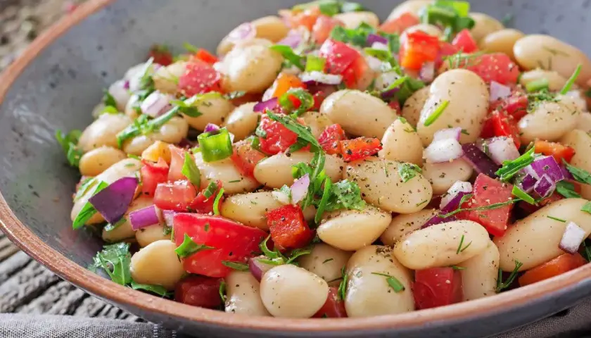 Insalata di fagioli bianchi, pomodori, cipolla rossa e erbe fresche in una ciotola rustica. Un piatto colorato e saporito.