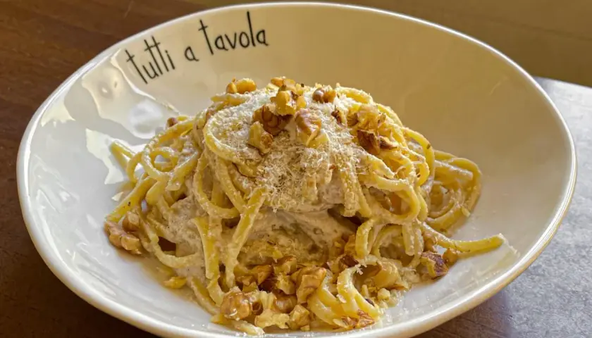 Pasta cremosa con pesto di noci, guarnita con noci tritate e parmigiano grattugiato. Un piatto invitante per tutti a tavola.