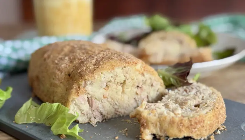 Polpettone di tonno dorato e croccante, tagliato a fette, servito con insalata fresca.
