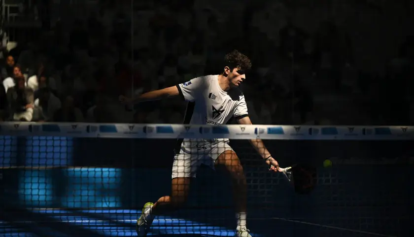 Arturo Coello in azione, colpisce la palla con la racchetta da padel, concentrato sul campo blu illuminato.