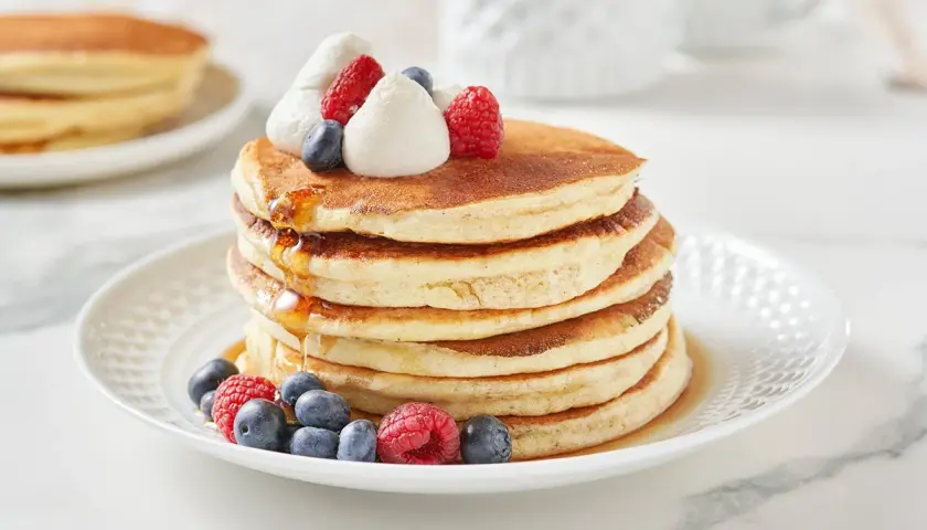 Pancakes dietetici con panna montata, mirtilli e lamponi, inzuppati nello sciroppo d'acero.