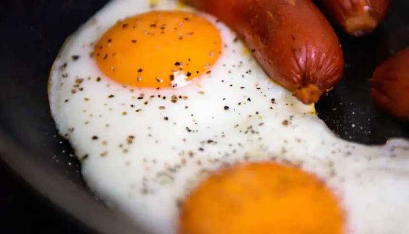 Due uova occhio di bue con pepe nero e salsicce in padella.