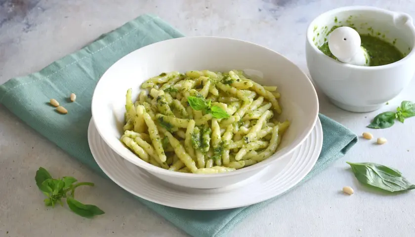 Un piatto di pasta al pesto fresco, con basilico e pinoli sparsi, pronto per essere gustato.