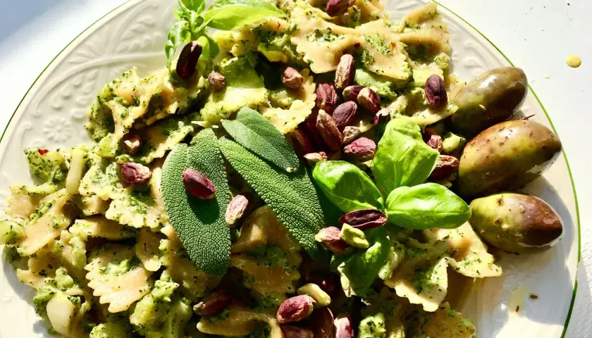 Farfalle condite con un saporito pesto di salvia, guarnite con pistacchi, basilico e olive verdi.