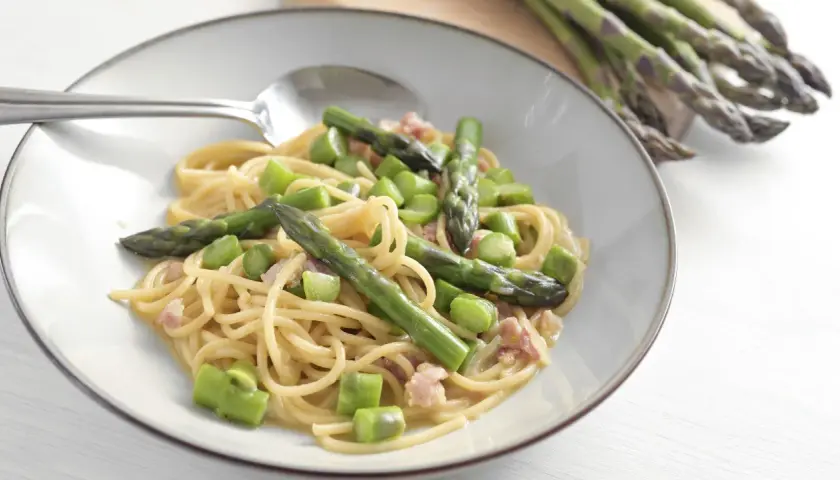 Un piatto di spaghetti con asparagi freschi e cubetti di speck croccante, condito con una cremosa salsa.