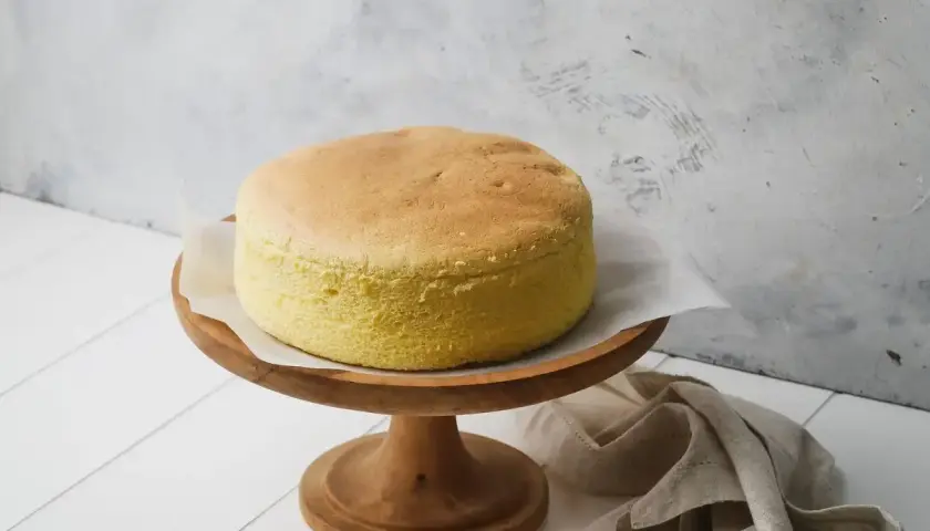 Una soffice torta con albumi, dorata e leggera, su un alzata di legno. Perfetta per una colazione o merenda.