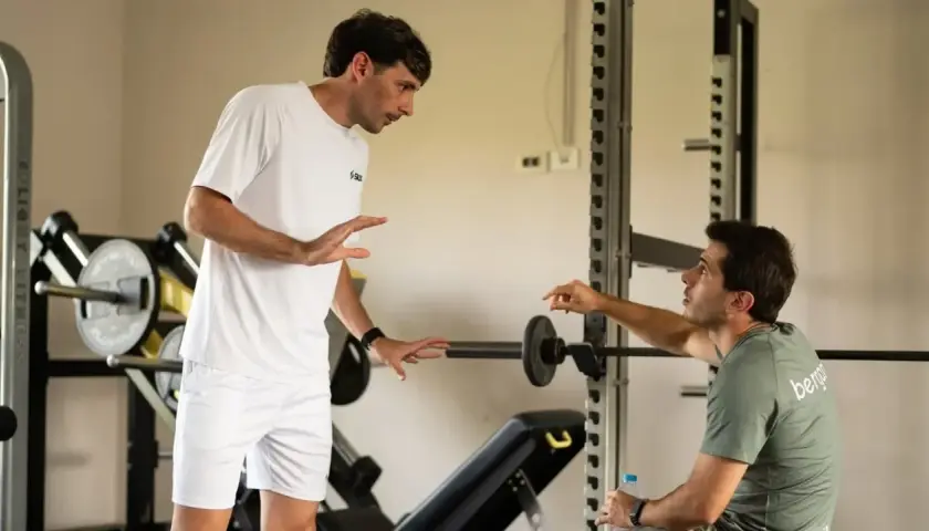 Due uomini discutono in palestra, uno in bianco, l'altro con maglia "bergamini padel".