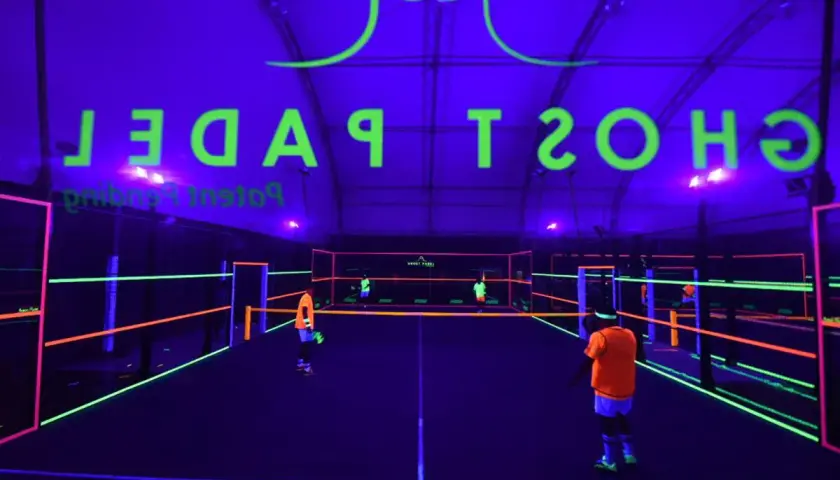 Campo da padel al neon con logo "Ghost Padel" e giocatori in azione.