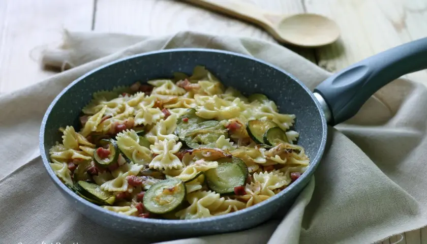 Farfalle con zucchine e pancetta croccante, un piatto semplice e gustoso pronto in padella.