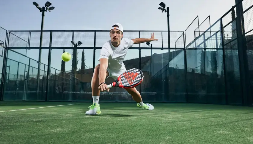 Ale Galán in azione, con le sue scarpe da padel che spiccano sul campo verde. Colpisce la palla con determinazione.