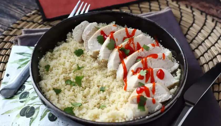 Delizioso pollo in padella a fette, servito su couscous e guarnito con salsa piccante e coriandolo fresco.