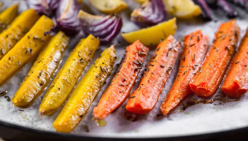Carote gialle e arancioni, cipolle rosse e patate dorate, condite con erbe aromatiche, pronte per essere gustate come deliziose verdure miste al forno.