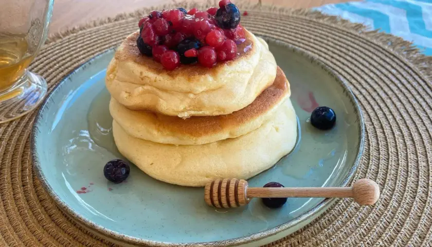 Pancake ricetta: soffici pancake impilati, guarniti con frutti di bosco e miele, pronti per essere gustati.