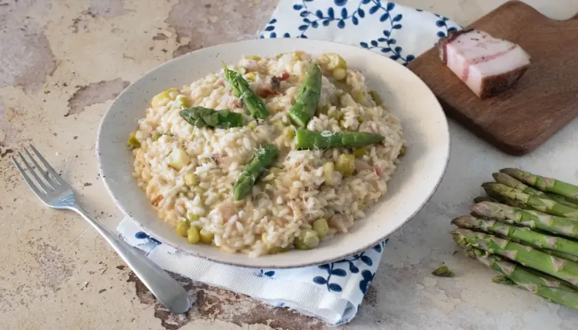 Un cremoso risotto con asparagi e pancetta, guarnito con punte di asparagi freschi e una spolverata di parmigiano.