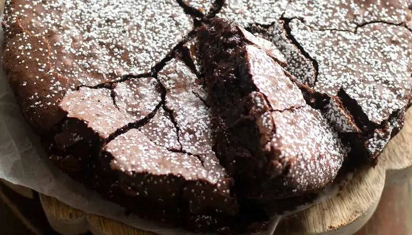 Torta al cioccolato fondente, con una crosta screpolata e cosparsa di zucchero a velo, pronta per essere gustata.