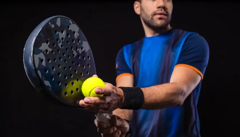 Giocatore di padel con racchetta e pallina, pronto a migliorare il suo gioco.