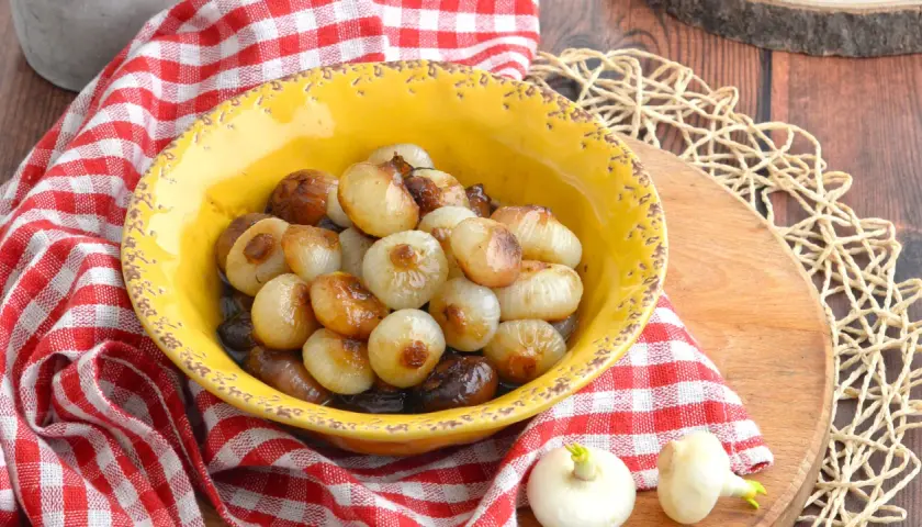 Cipolline caramellate in agrodolce, servite in una ciotola gialla con tovagliolo a quadri rossi.