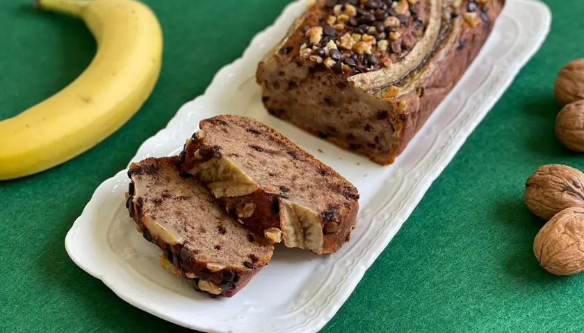 Delizioso banana bread light con gocce di cioccolato e noci, guarnito con banana e servito su un piatto bianco.