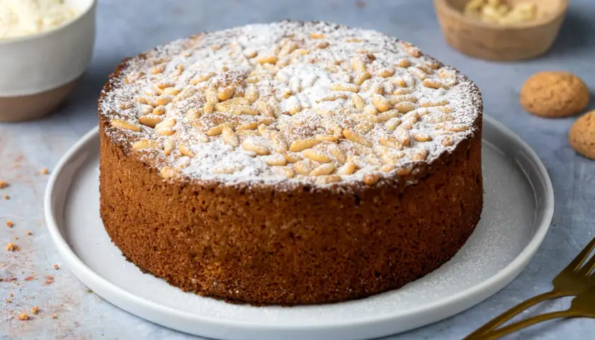 Torta soffice con farina di mandorle, cosparsa di pinoli e zucchero a velo.